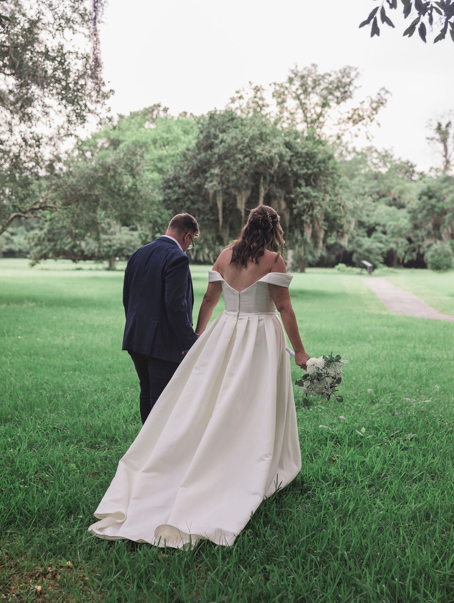 Bride and groom hand in hand taking a romantic walk through a picturesque Charleston, SC. park on their wedding day.