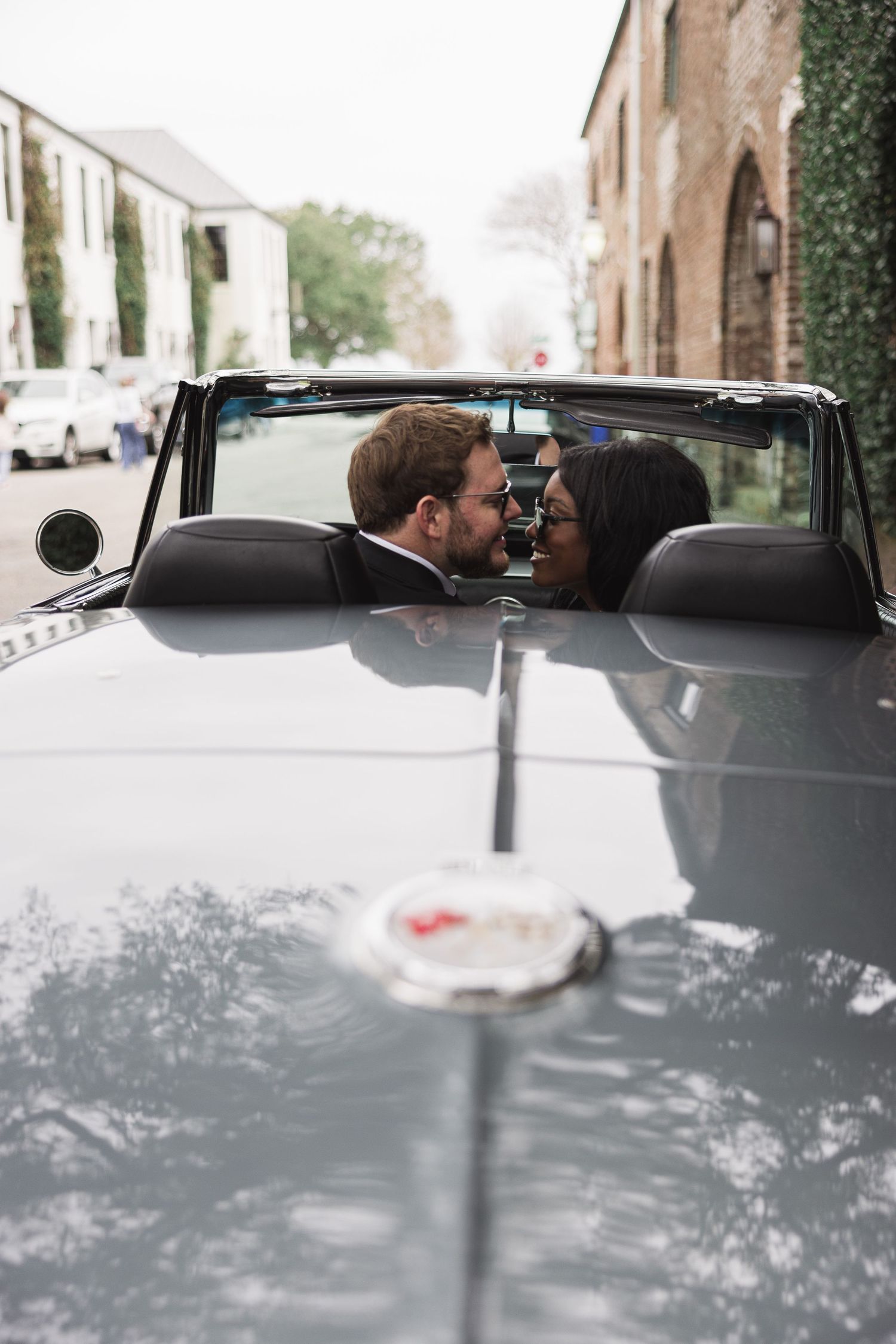 Engaged couple at the start of a new journey in a 66 Corvette on the cobblestone streets of Charleston, SC. in a warm embrace.