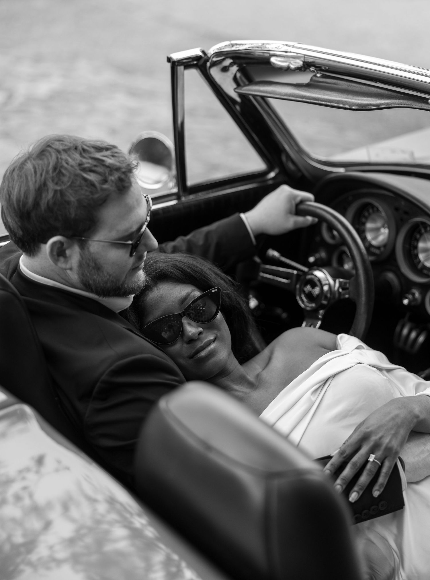 Engaged couple at the start of a new journey in a 66 Corvette on the cobblestone streets of Charleston, SC. in a warm embrace.