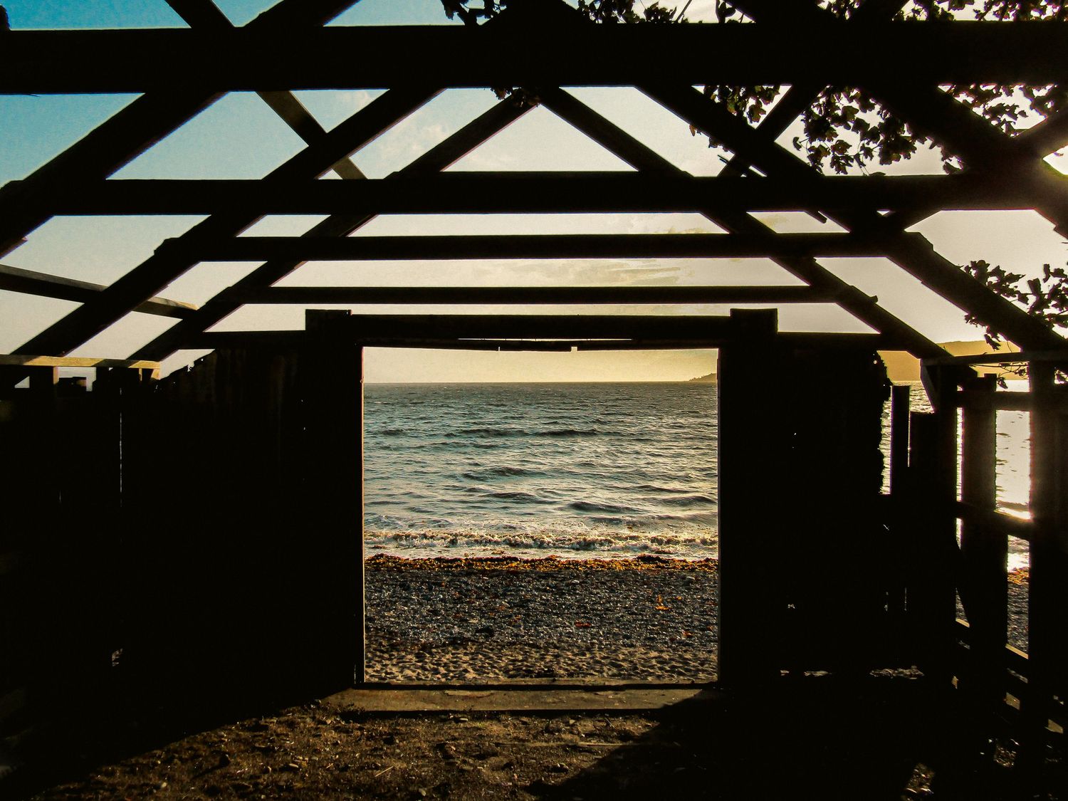 Fine art dramatic silhouette photograph looking through old boathouse towards the ocean, framed wall art prints and downloads.
