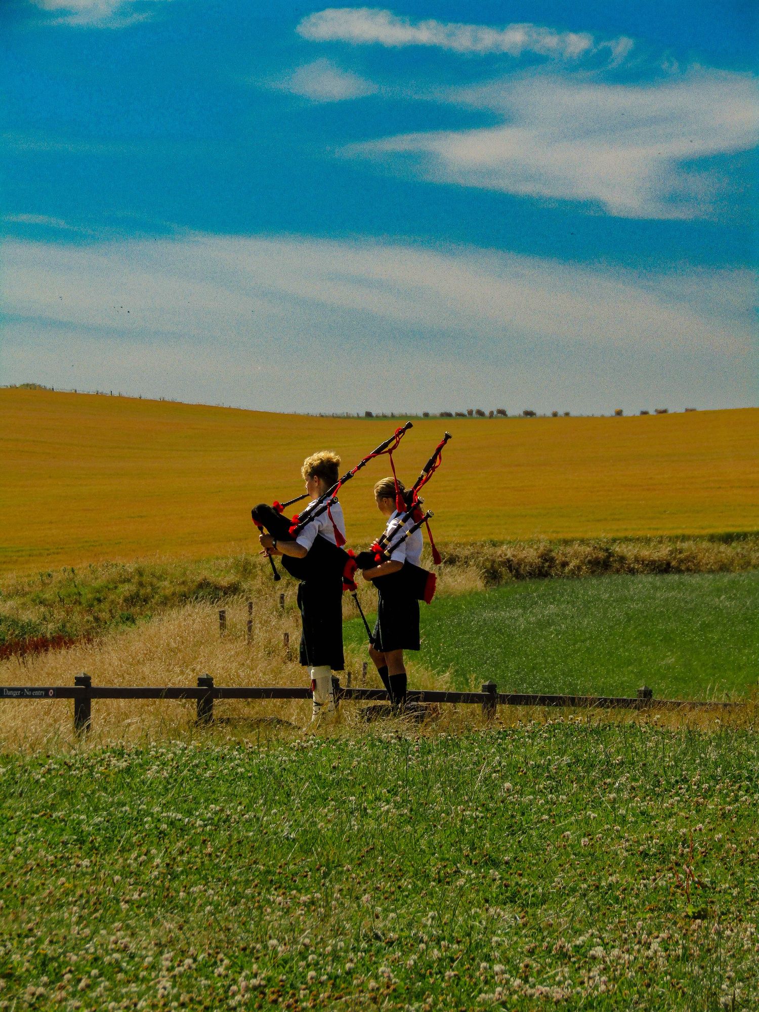Young Bagpipers at Dunnottar Castle with blue sky, yellow and green fields.