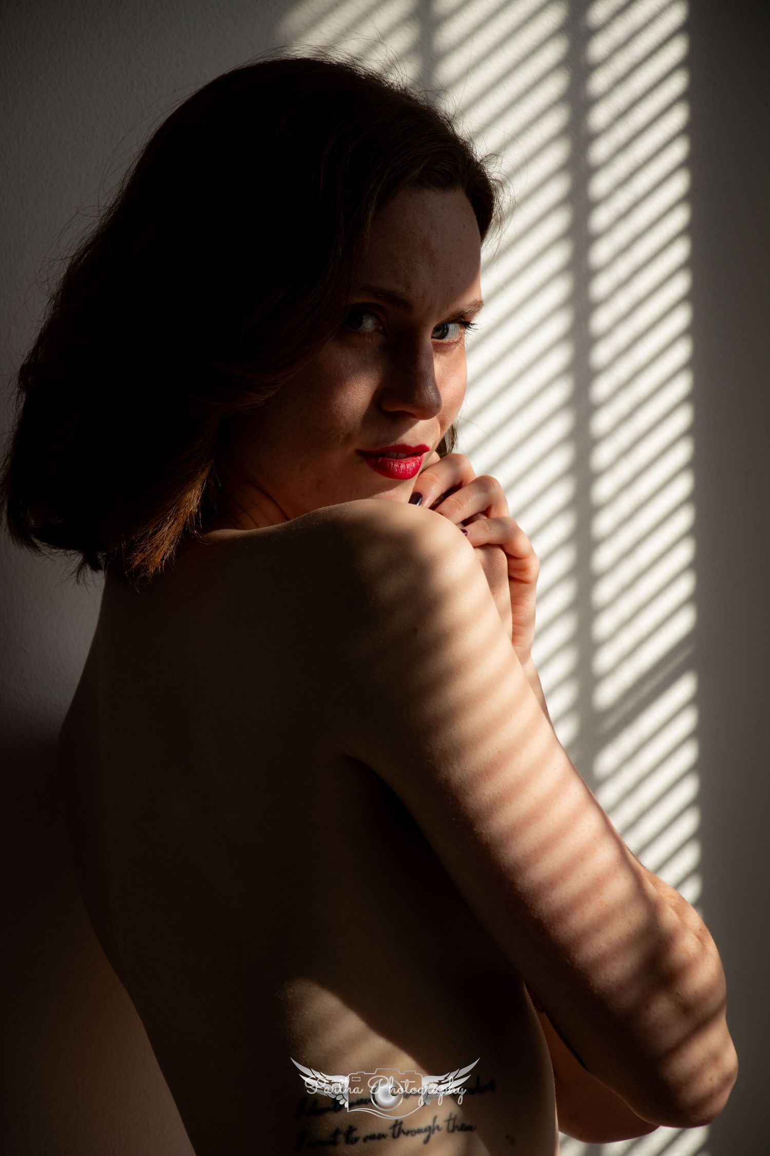 Artistic boudoir portrait with dramatic window light and shadow patterns.