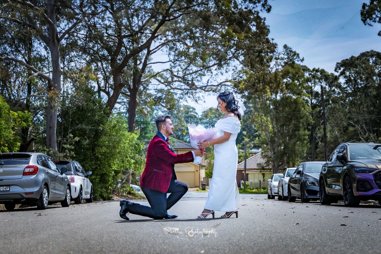Wedding proposal scene with person kneeling in a parking lot surrounded by cars.