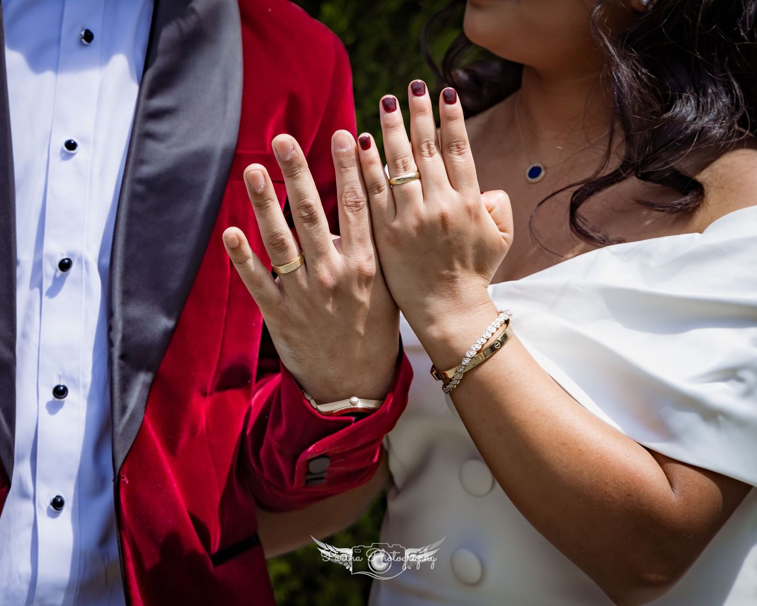 Close-up of hands displaying wedding rings against a red and white formal attire background.