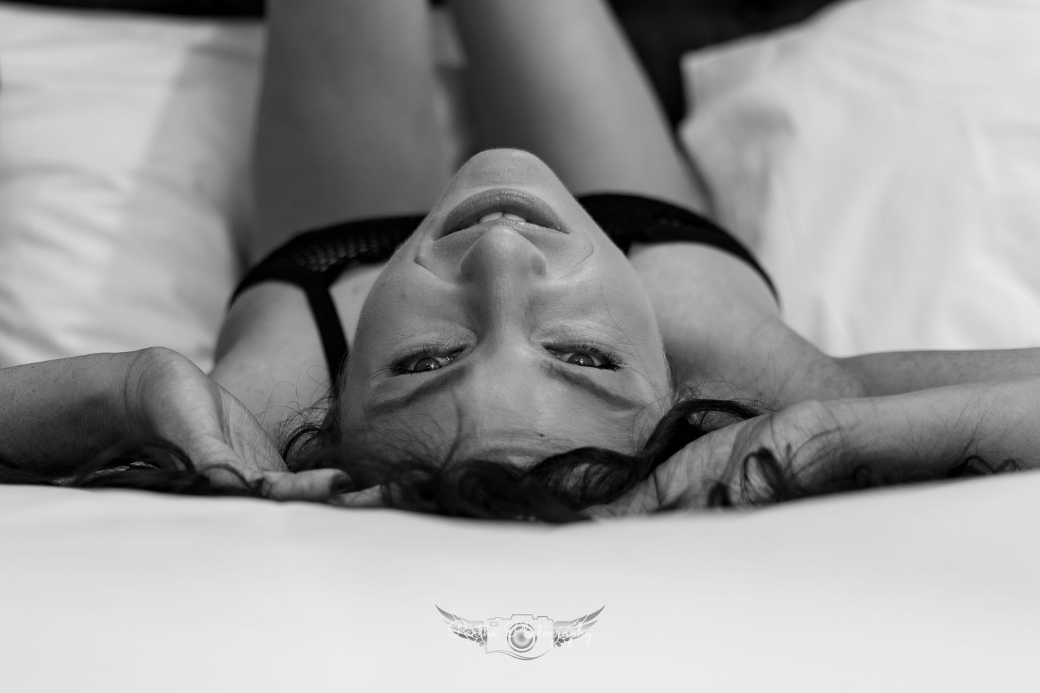 Black and white artistic portrait of someone lying on white bedding with dramatic shadows.