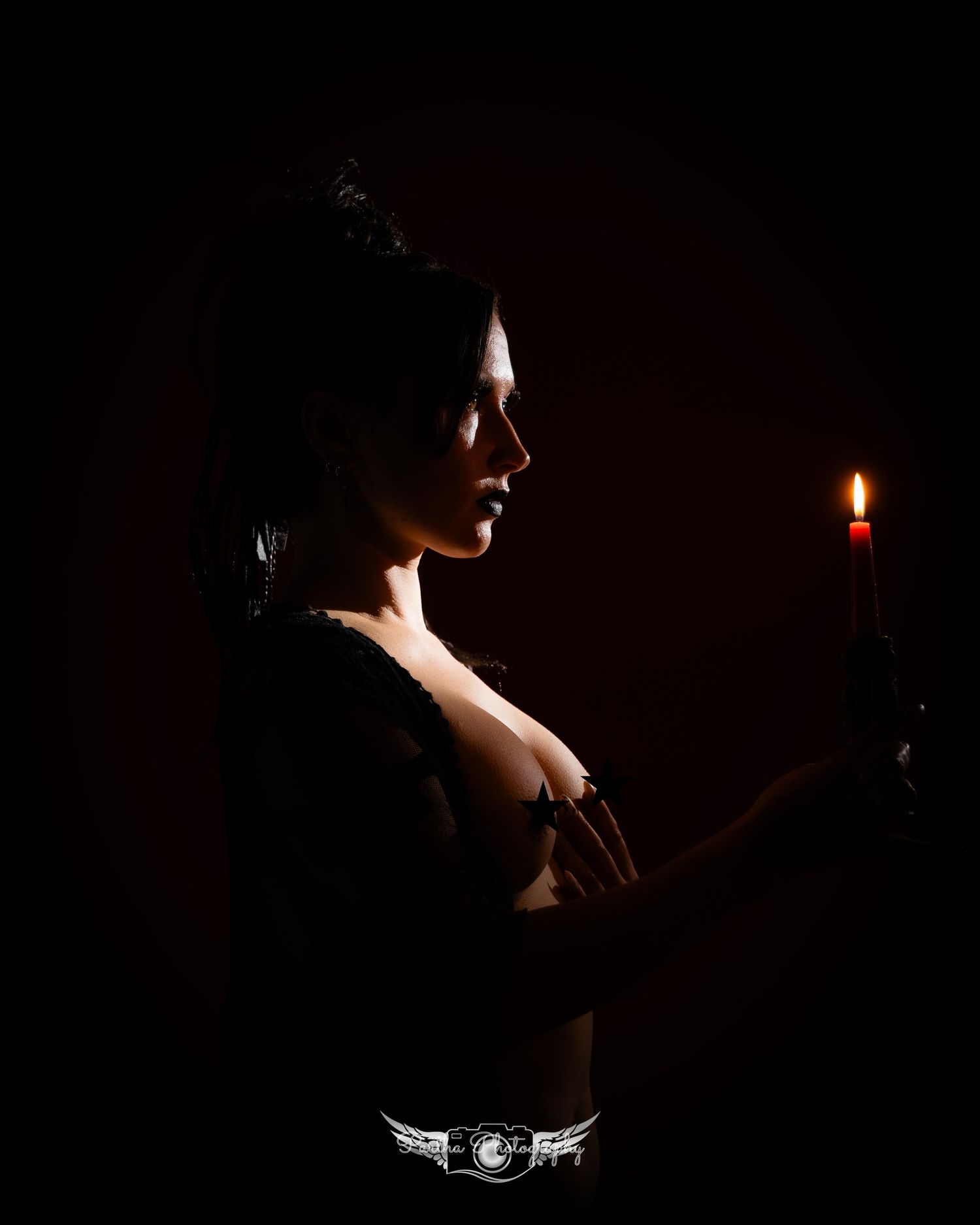A silhouetted figure stands in dramatic low light holding a lit candle, creating a moody atmospheric scene.
