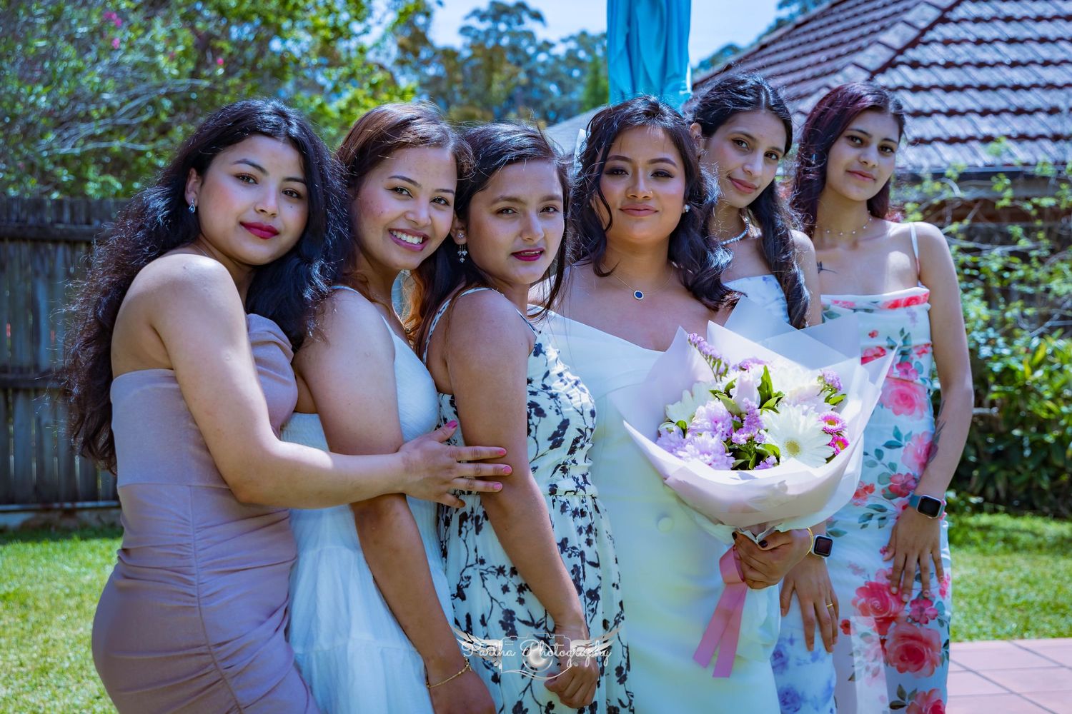 A group of bridesmaids in pastel dresses posing together with flowers in a garden setting.