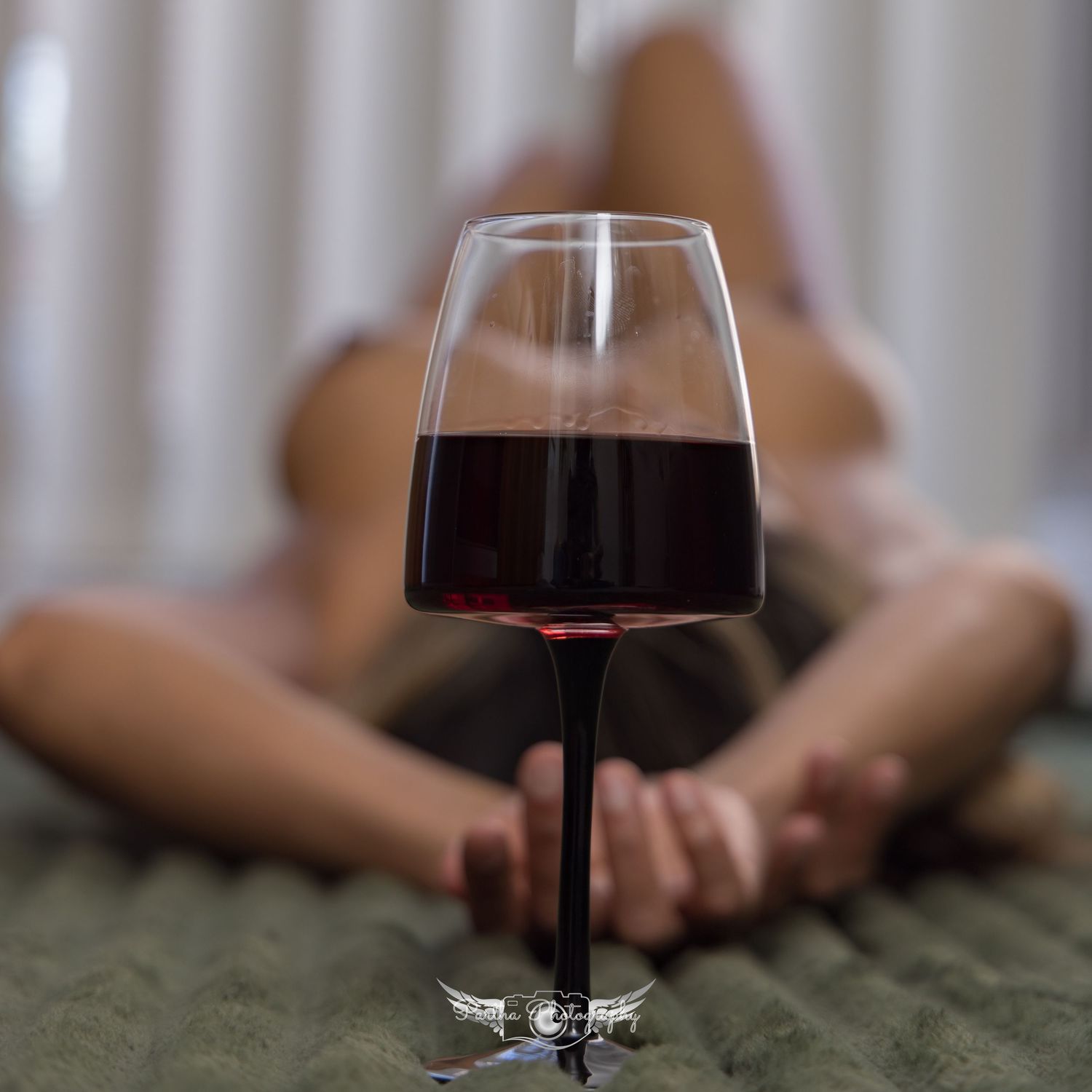 A glass of red wine in focus with a blurred background showing someone relaxing on a green surface.
