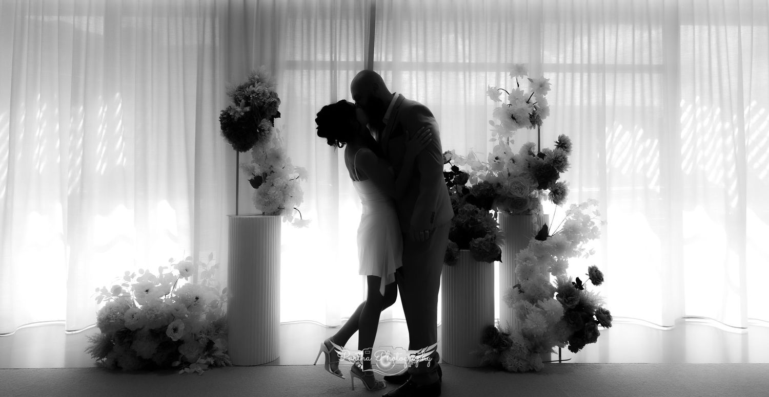 Silhouette of a couple embracing in front of white curtains with artistic black smoke effects.