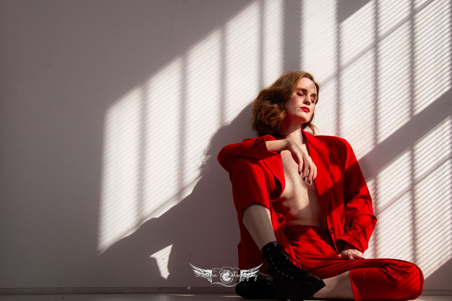 Sunlit portrait in red jacket against white wall with dramatic window shadows.