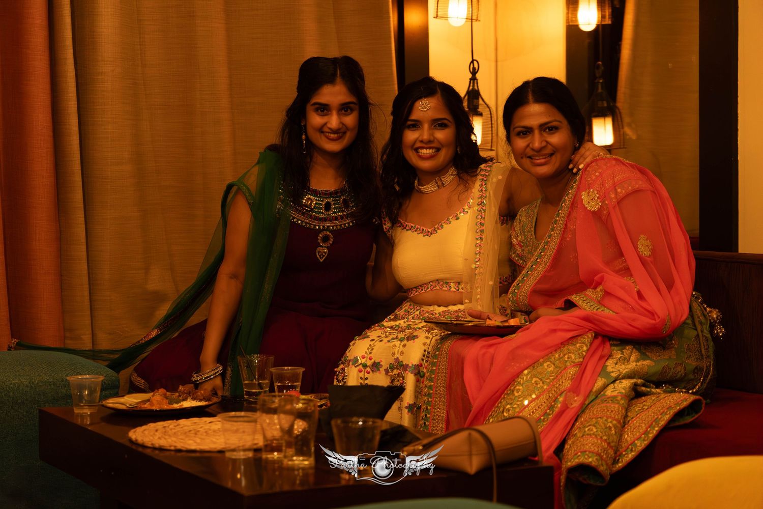 Three women in traditional Indian attire sitting together at an evening celebration.