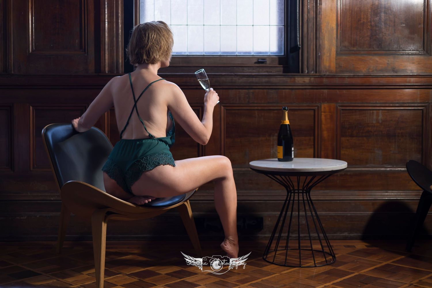 A person sits alone in a dimly lit wooden room with vintage furniture and window light.