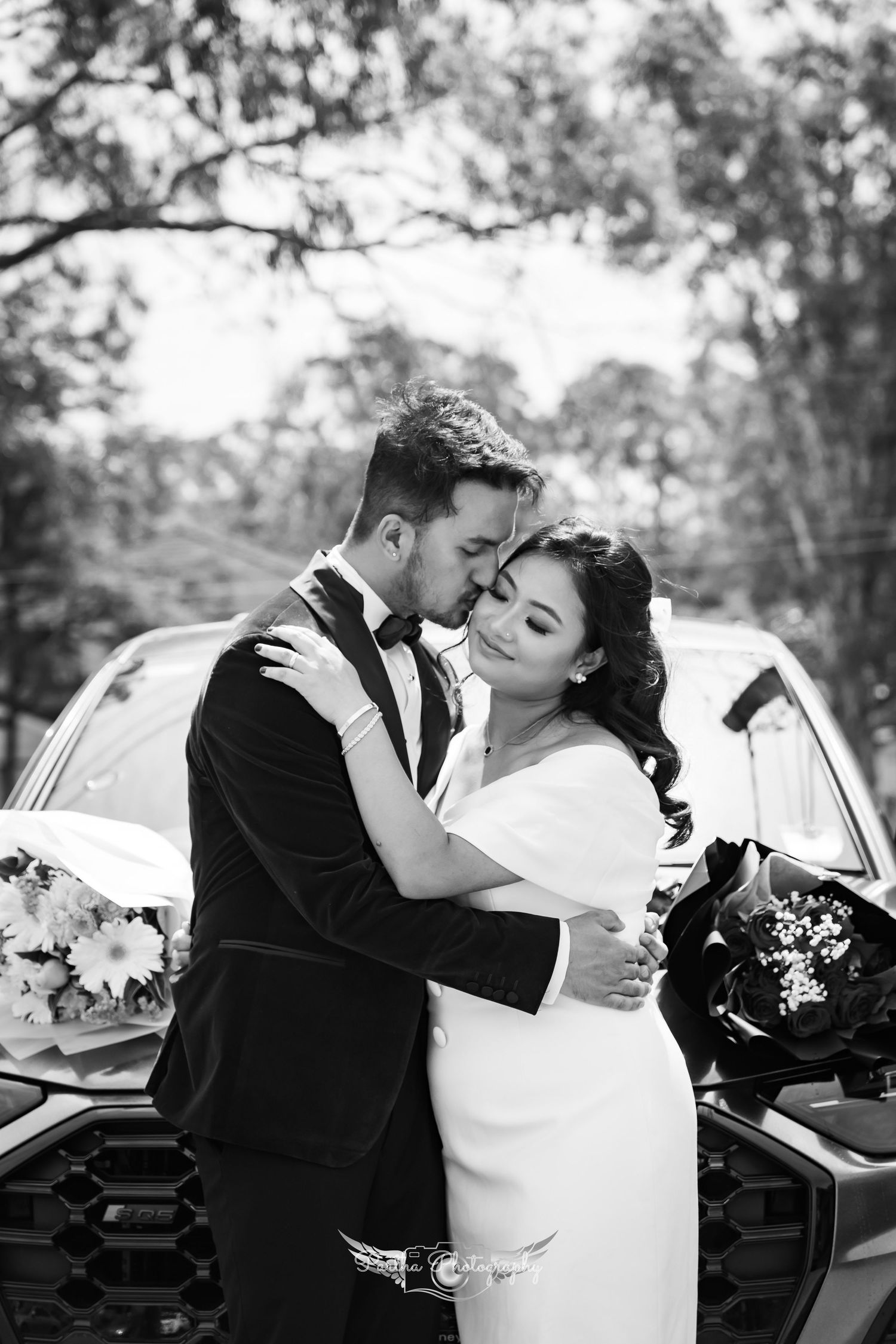 Black and white intimate portrait of couple embracing by car during wedding photoshoot.