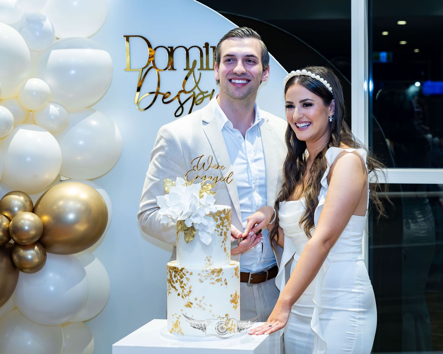 Couple cutting their elegant white and gold wedding cake with balloon decorations.