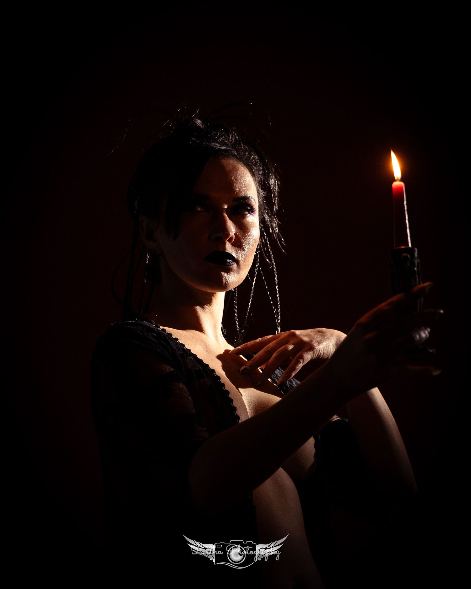 Moody portrait of a figure holding candle with dramatic lighting against dark background.
