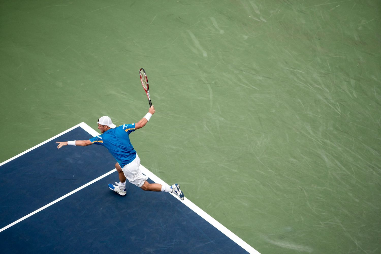 A tennis player diving for a shot on a green and blue court surface.