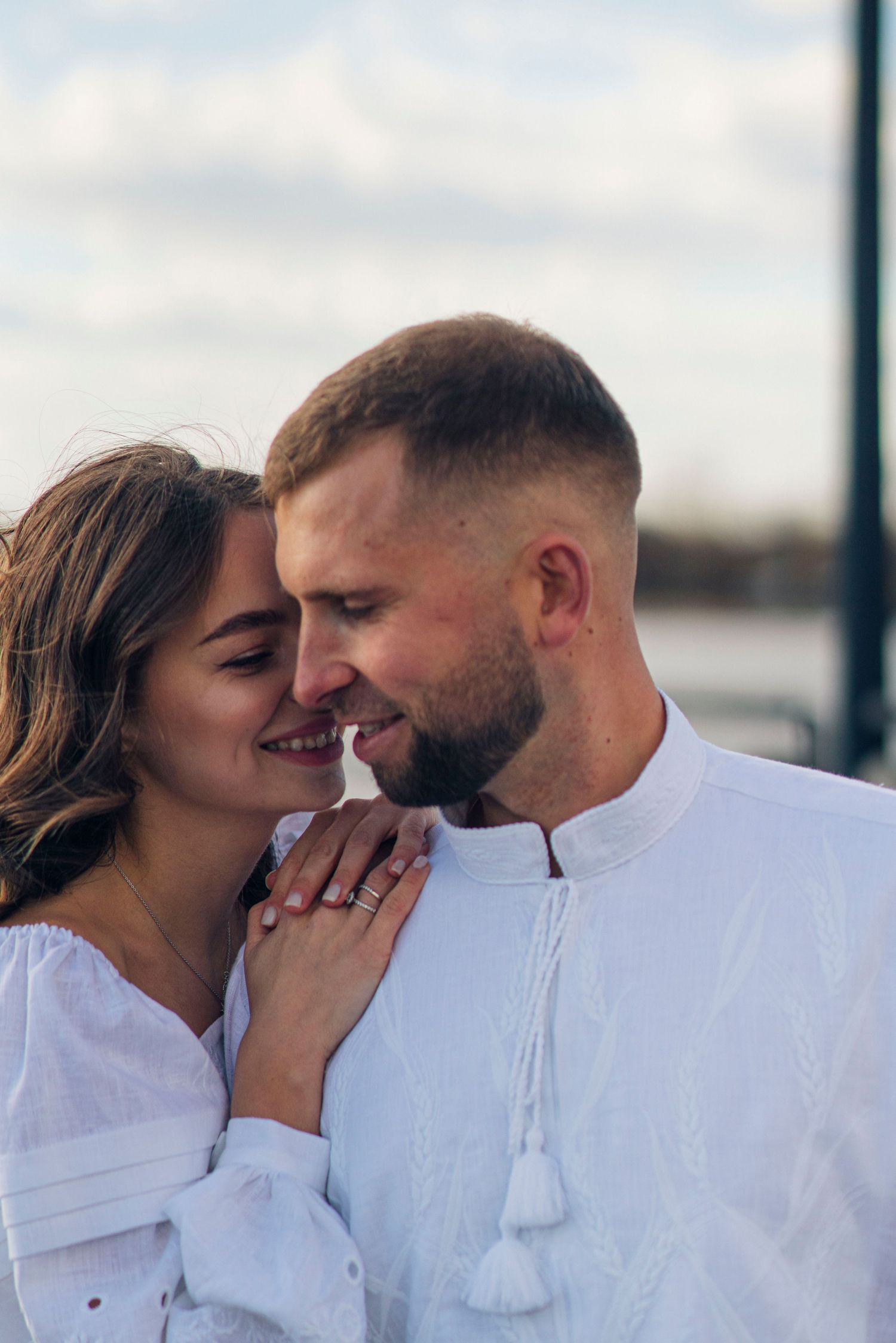 A romantic couple in white outfits share an intimate moment outdoors.