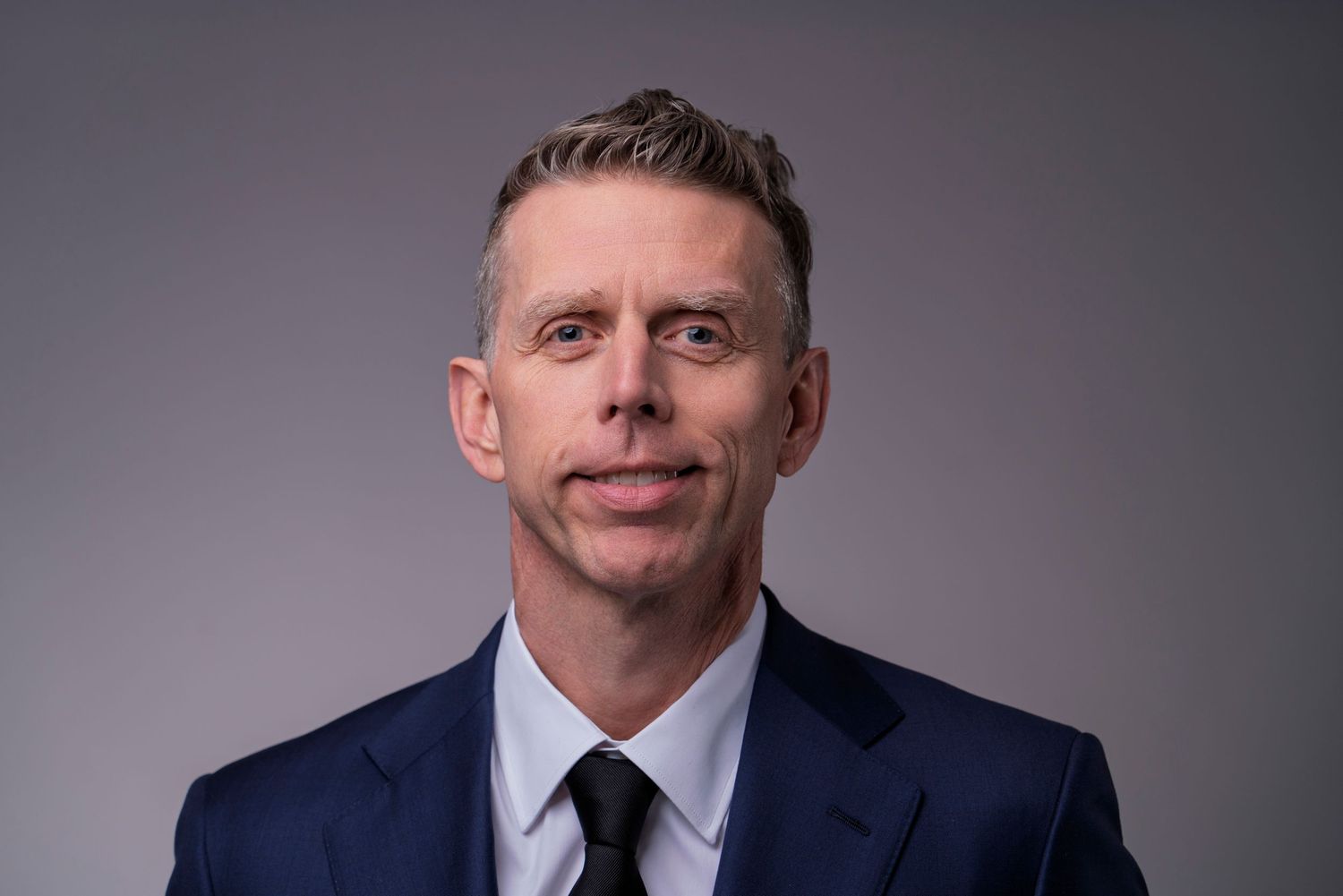Professional headshot series of a businessman in a dark suit against a gray background.