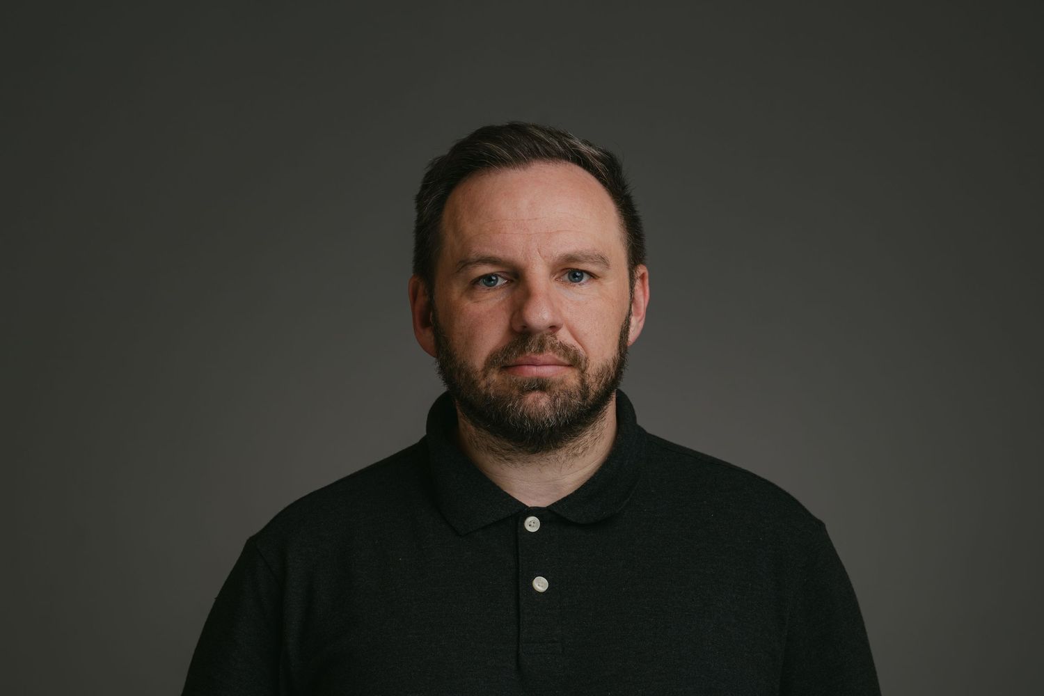 Portrait of a person in a black polo shirt against a dark studio background.
