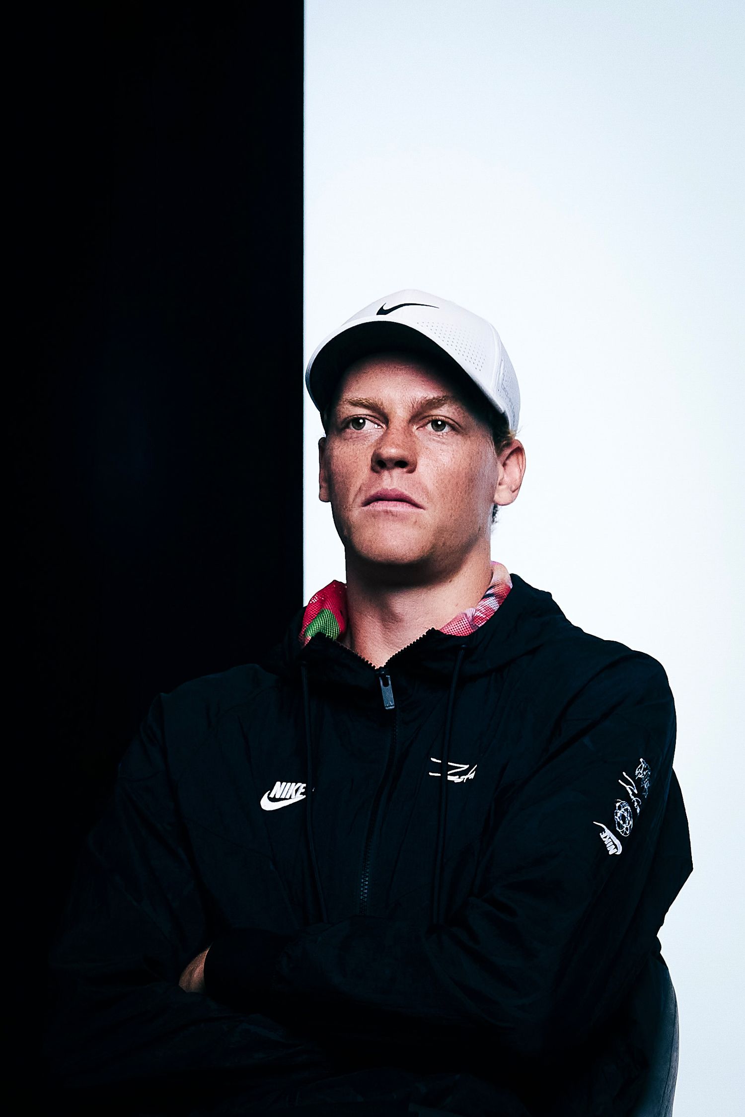 Athletic figure in Nike cap and black hoodie poses against contrasting black and white backdrop for dramatic portrait.