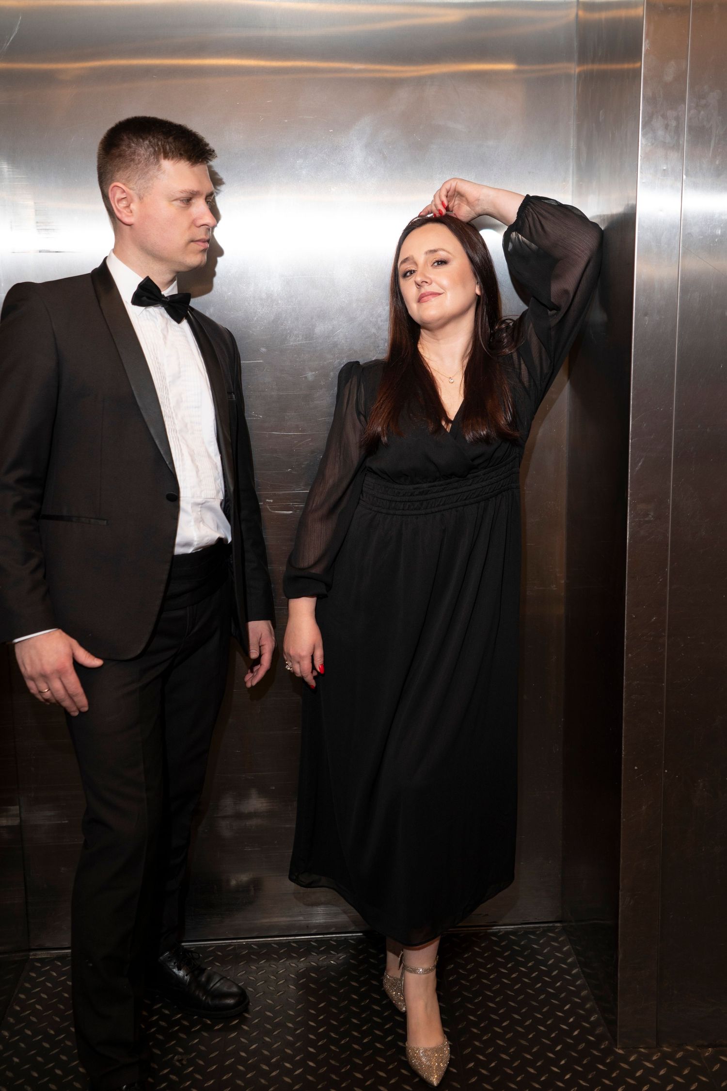 A couple in formal wear poses dramatically in an elevator setting.