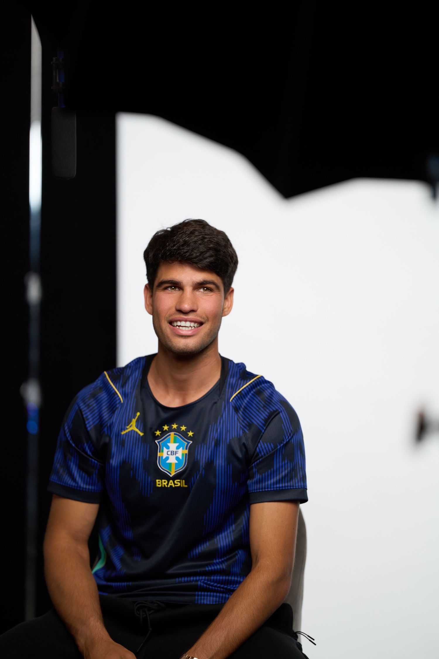 A person wearing a dark blue Brazil soccer jersey with yellow accents poses against a black background.