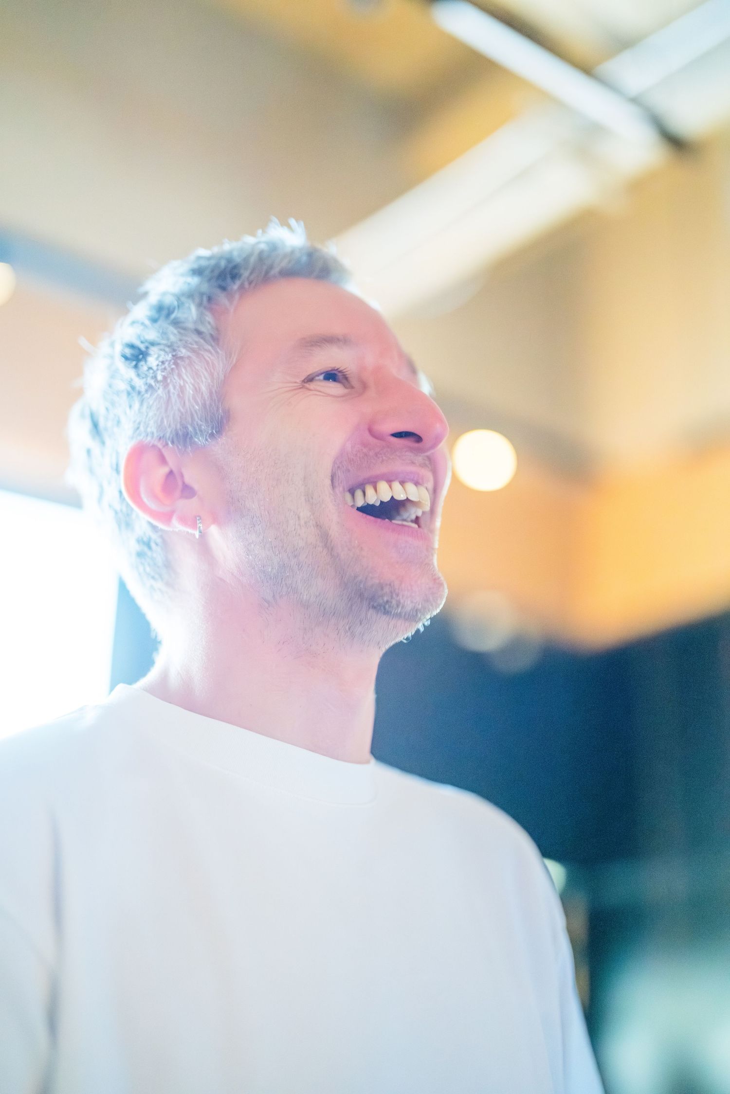 Happy middle-aged man with gray hair laughing joyfully in bright modern indoor setting.