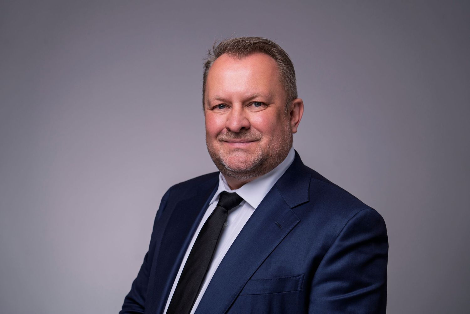 Professional headshot portrait of businessman in navy suit against gray background.