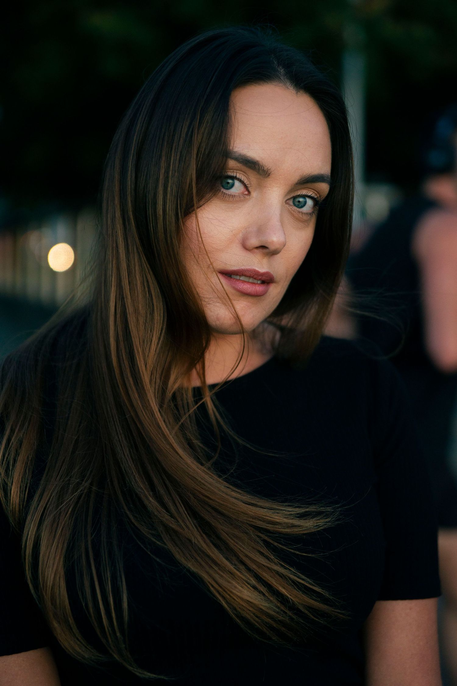 Beauty portrait of woman with long brown hair in black top against evening lighting.
