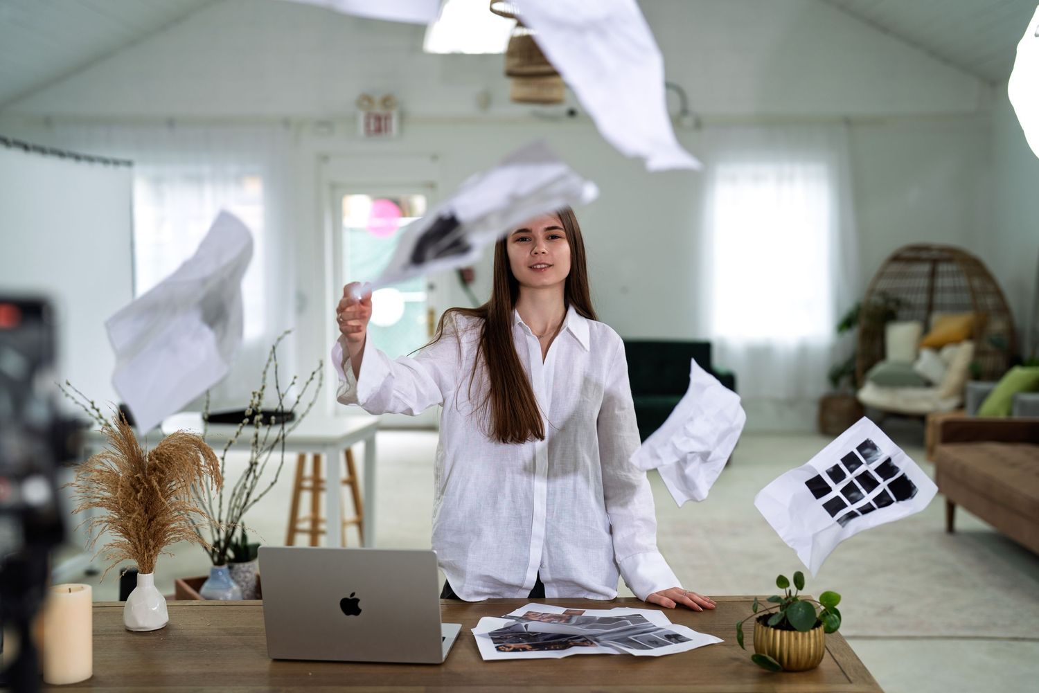 Modern office workspace with laptop, plants and white clothing visible.