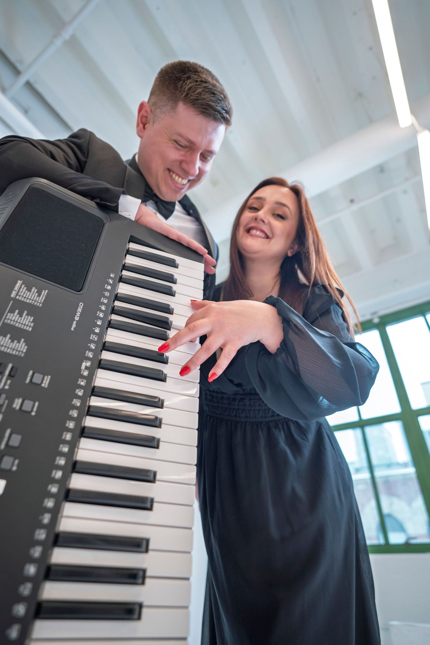 A couple poses playfully with piano keys in a bright modern setting.
