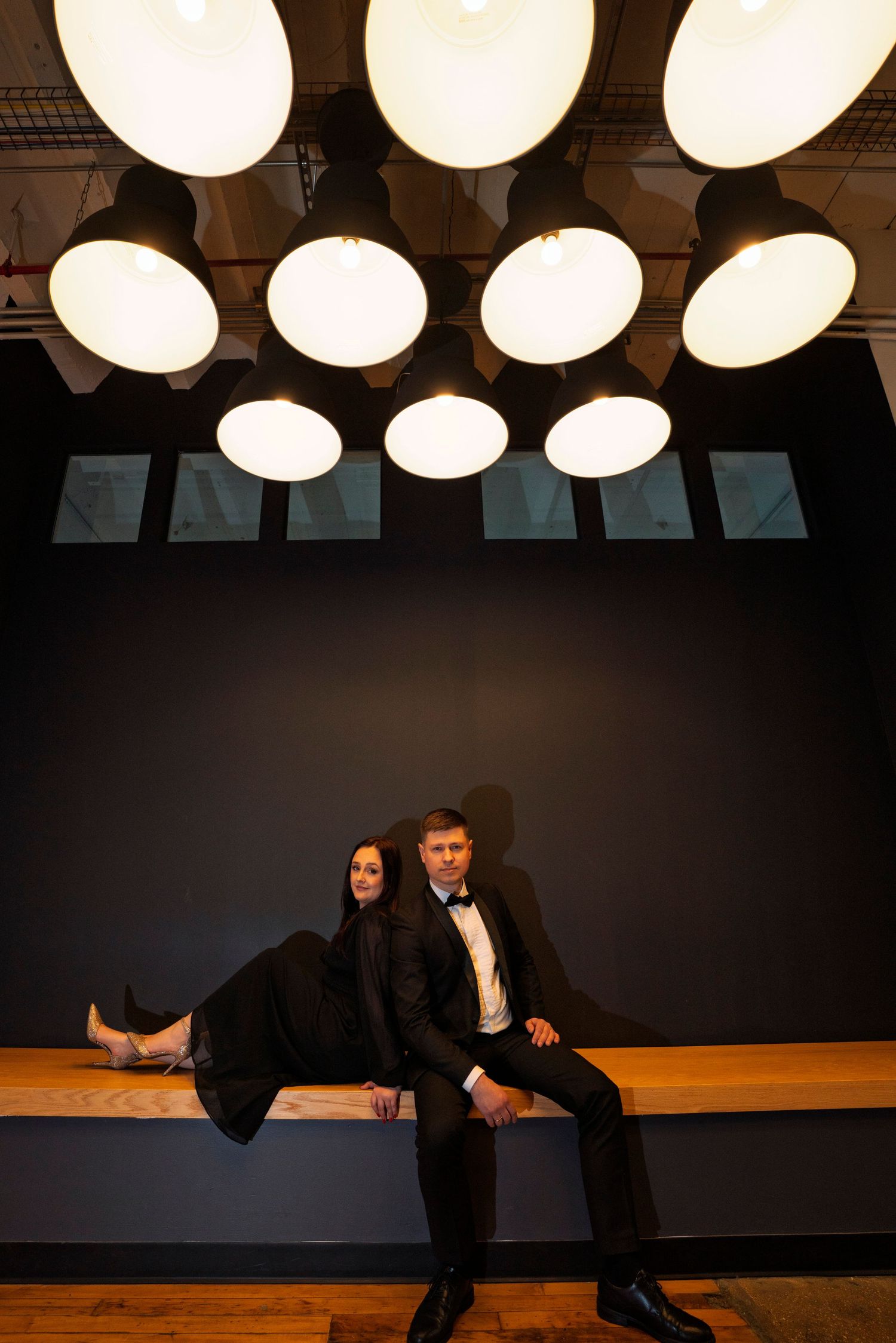 A couple poses beneath round ceiling lights in a dramatic setting.
