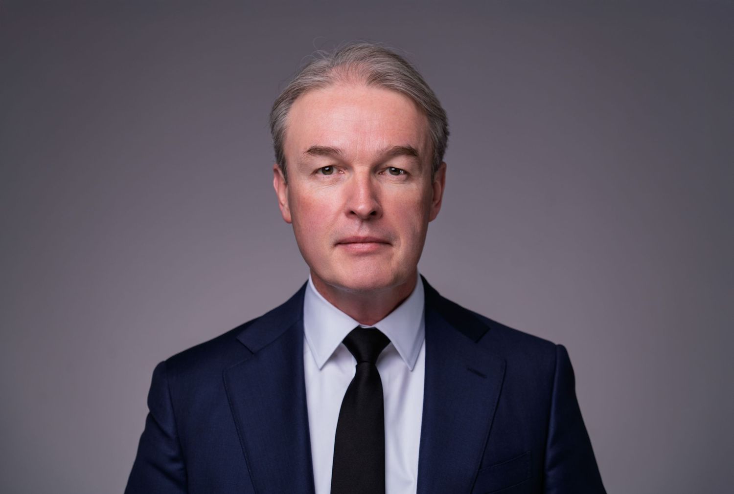 Corporate executive poses in formal business attire against studio backdrop.