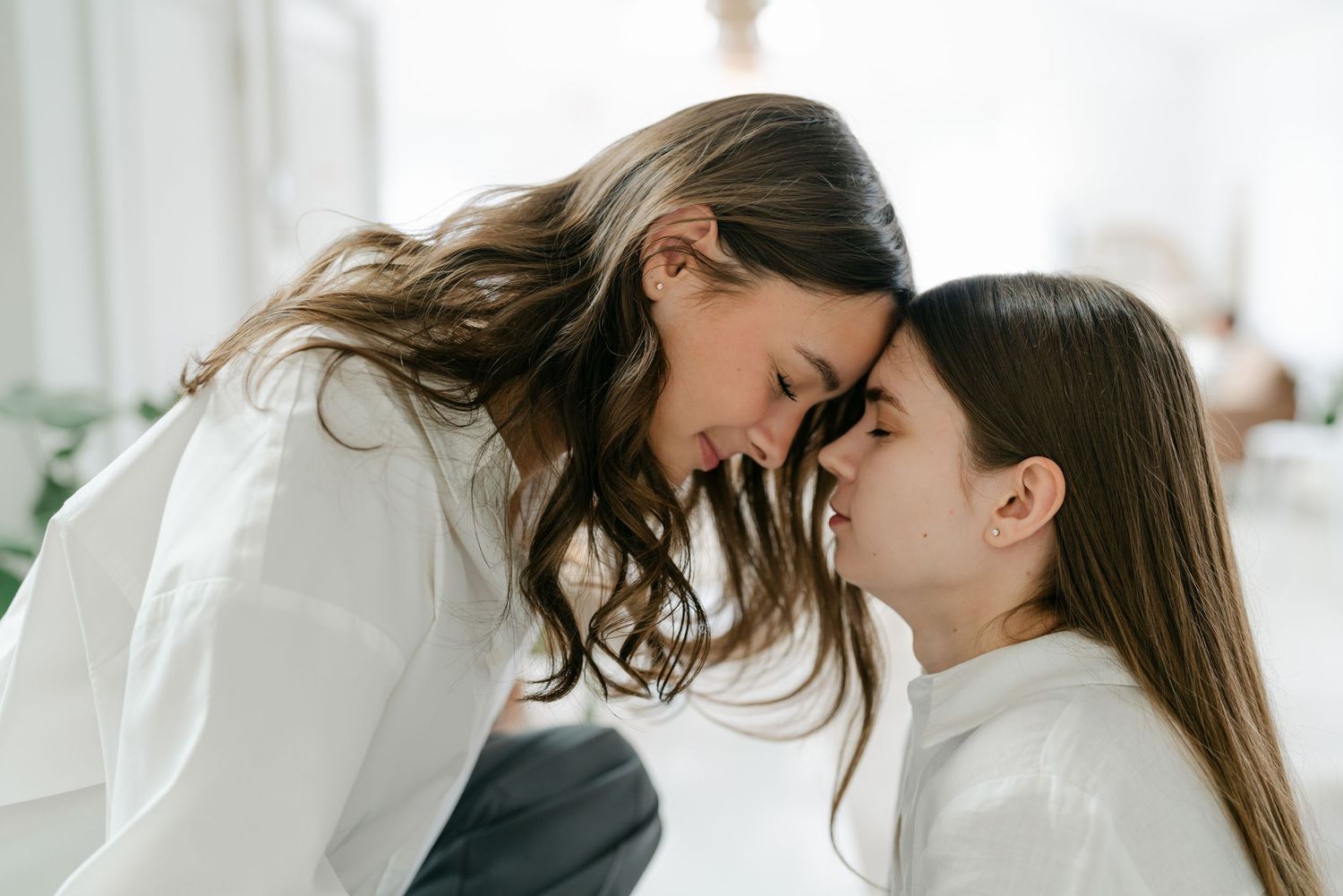 Two people in white outfits embrace in bright studio setting.