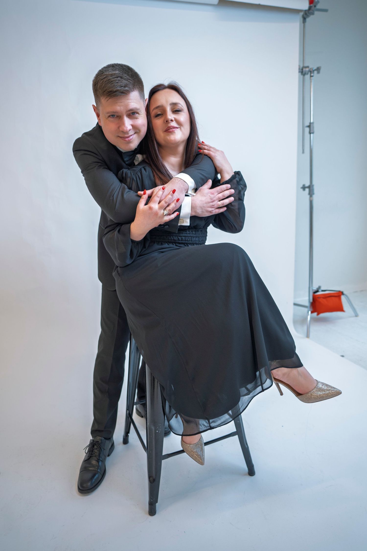 A couple performs playful poses with a chair in a photo studio.