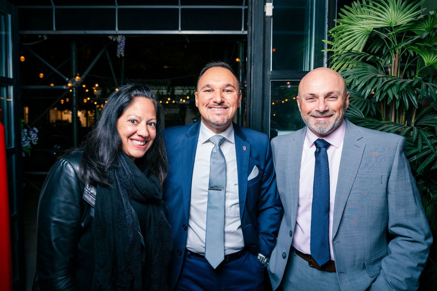 A group of people in business suits smile and pose together in front of a tropical plant backdrop.