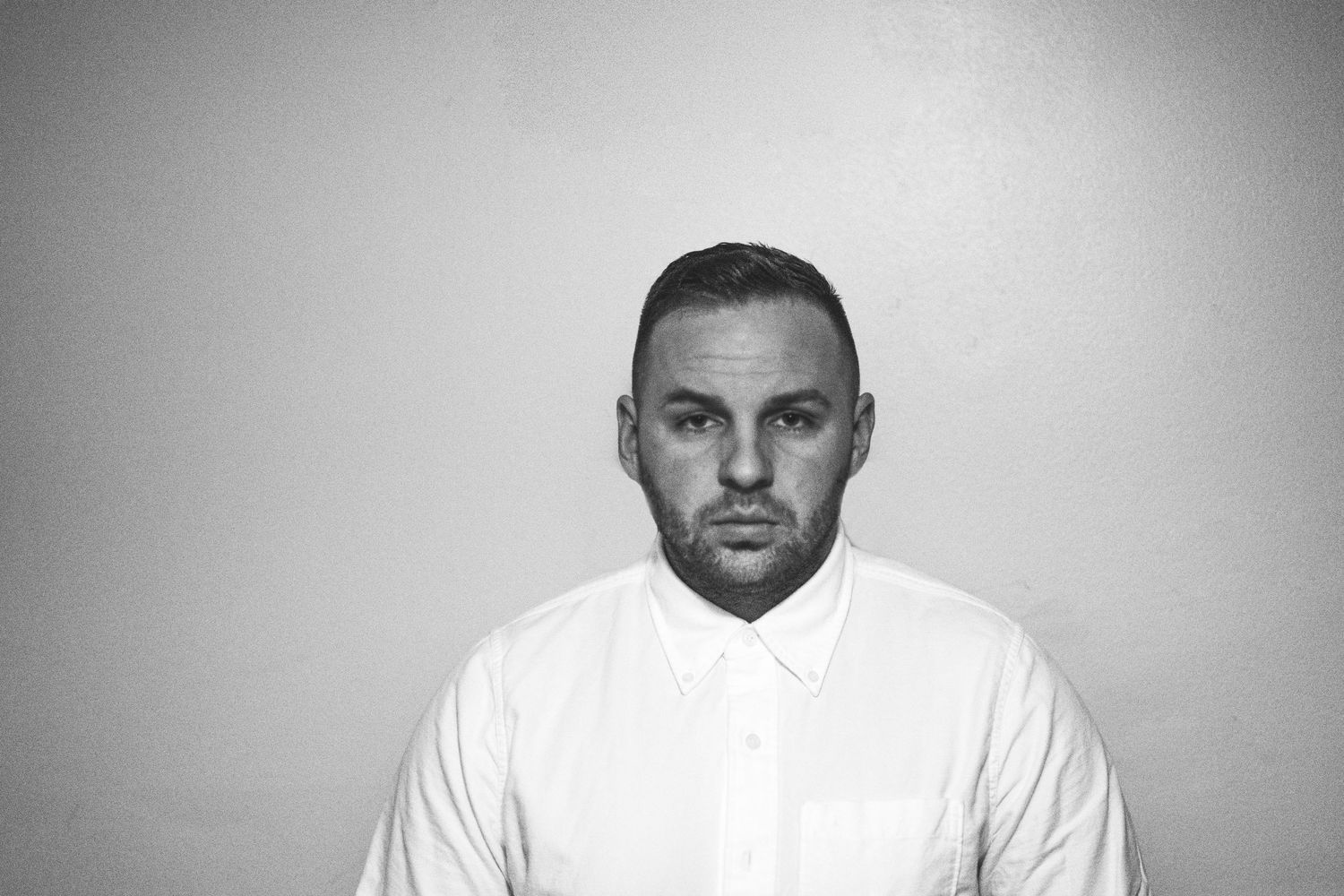 Studio portrait of a person in a white collared shirt against a gray background.
