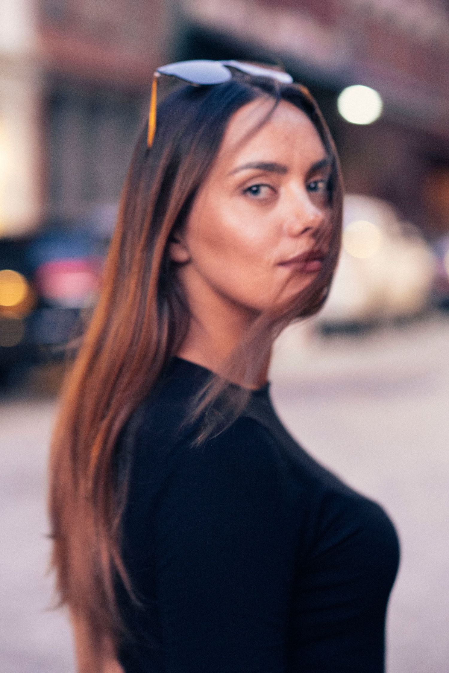 Portrait of young woman with long brown hair making playful expression on city street.