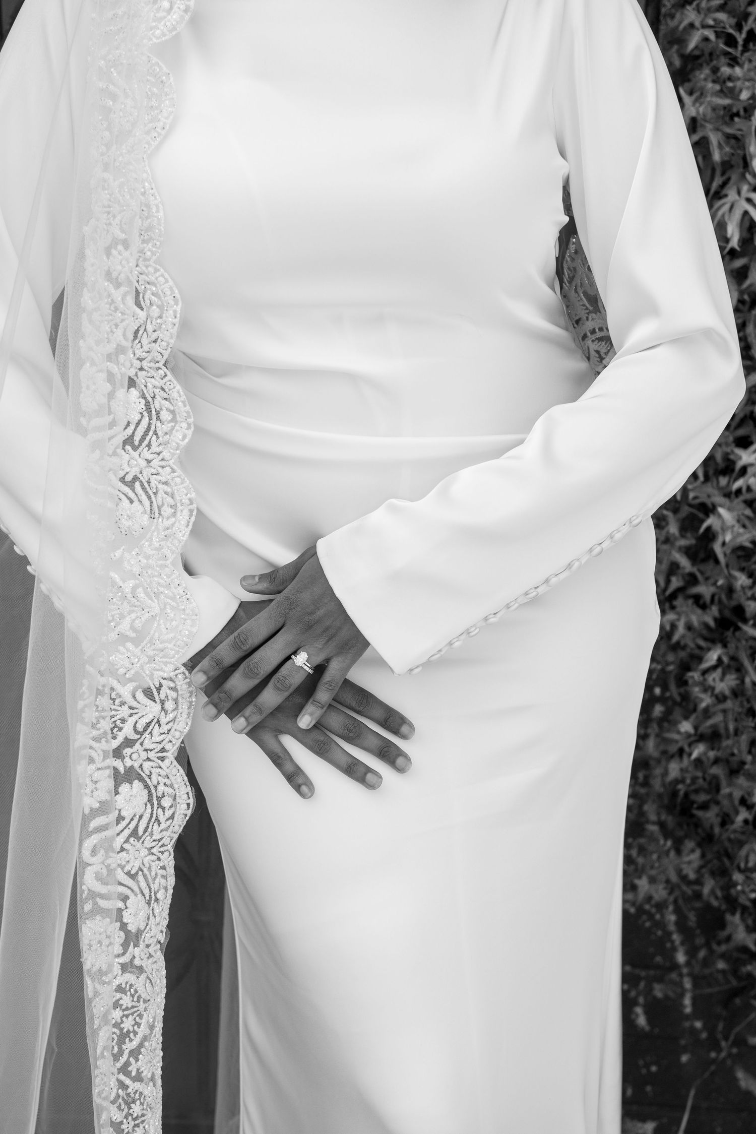 Close-up details of a white wedding dress sleeve with intricate lace embellishments and beading against a dark background.