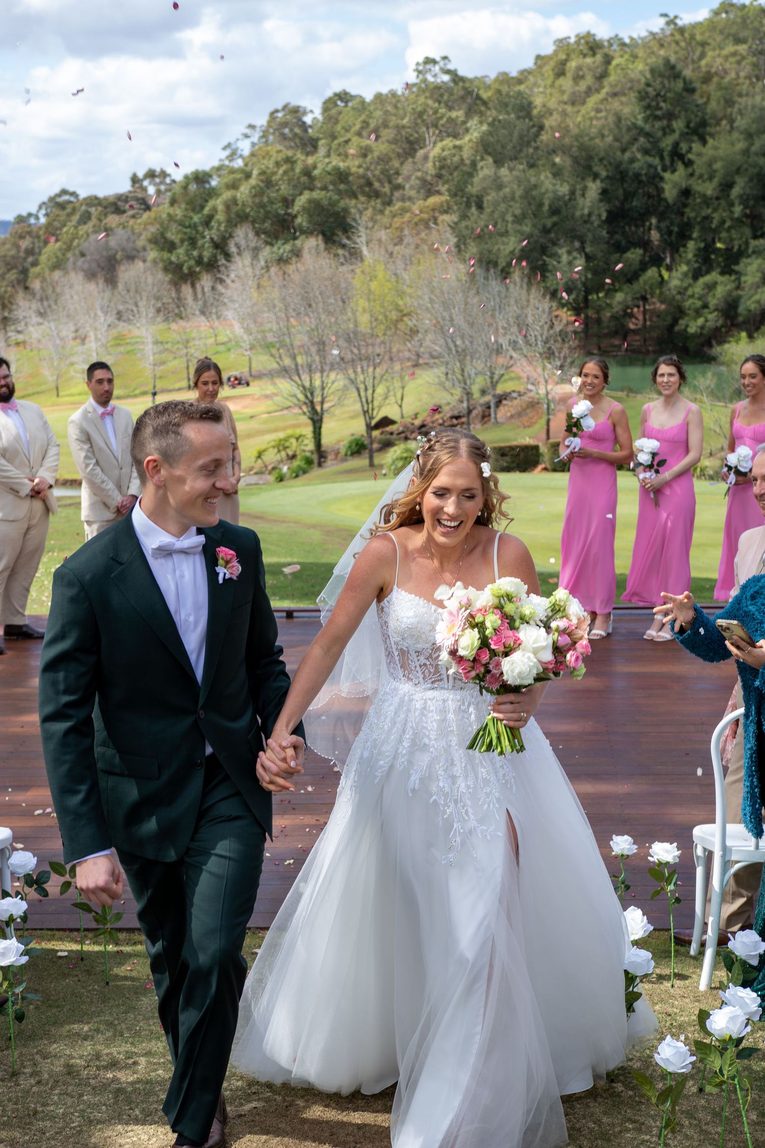 A joyful wedding ceremony takes place on a deck overlooking a scenic golf course with bridesmaids in pink dresses.