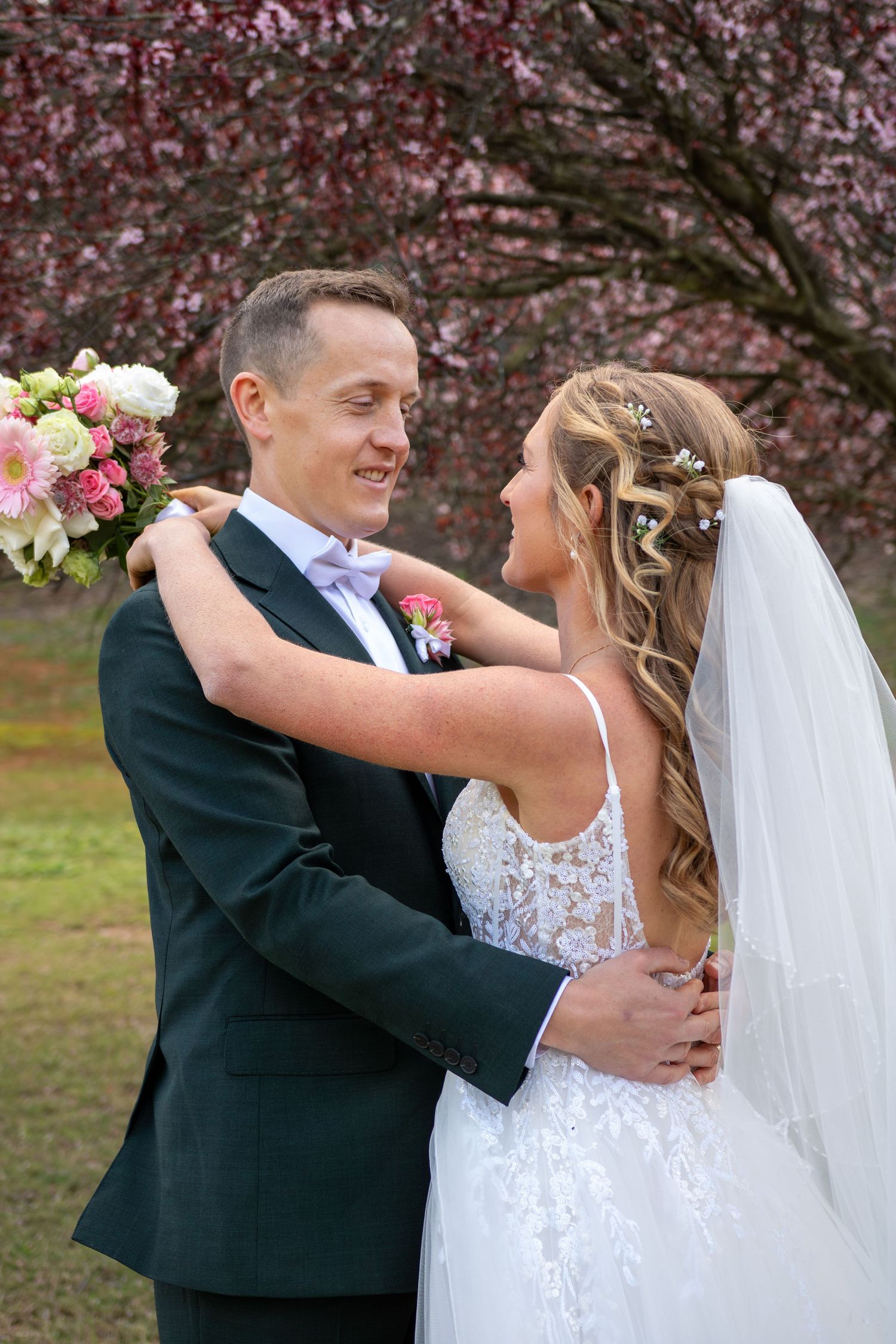 A romantic wedding couple embraces under blooming cherry blossoms during their spring outdoor photo session.