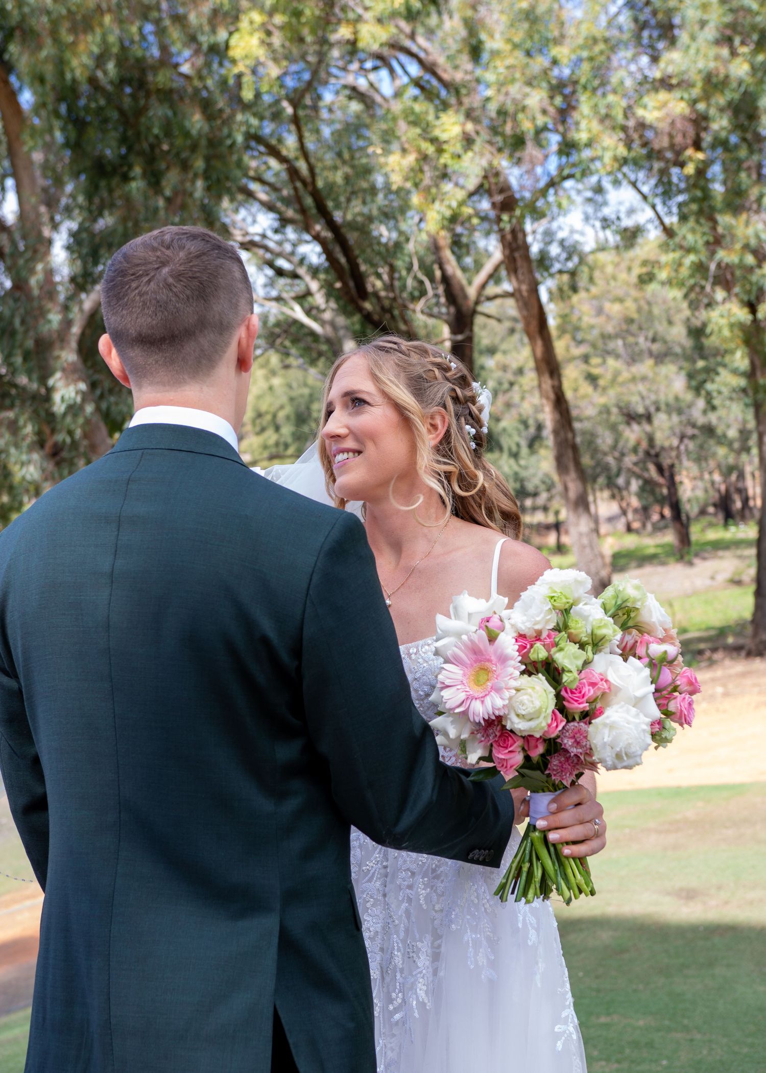 A couple shares a joyful moment at their outdoor wedding, with the bride holding a pink and white floral bouquet.