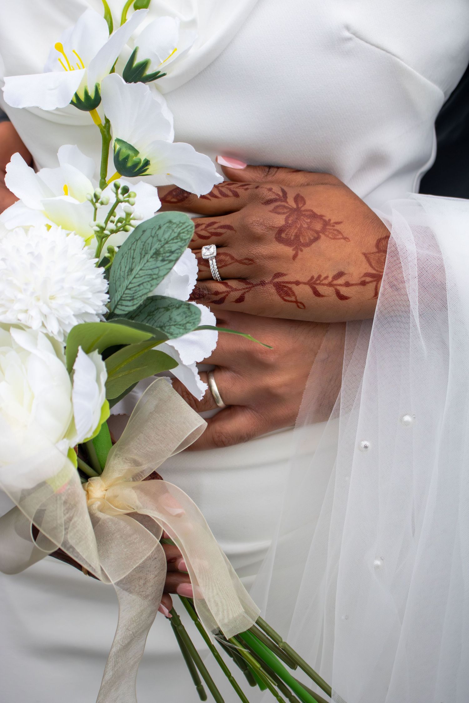 Close-up of hands holding an elegant white floral bouquet with delicate tulle wrapping at a wedding ceremony.