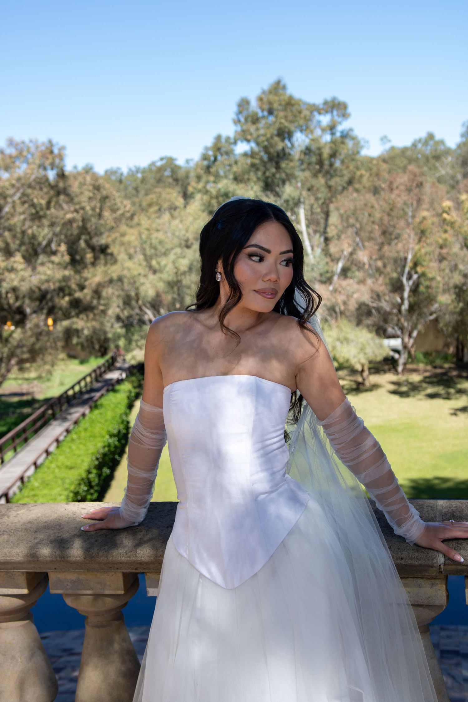 Romantic outdoor bridal photos showcasing a strapless white ballgown against a scenic garden backdrop with stone architecture.