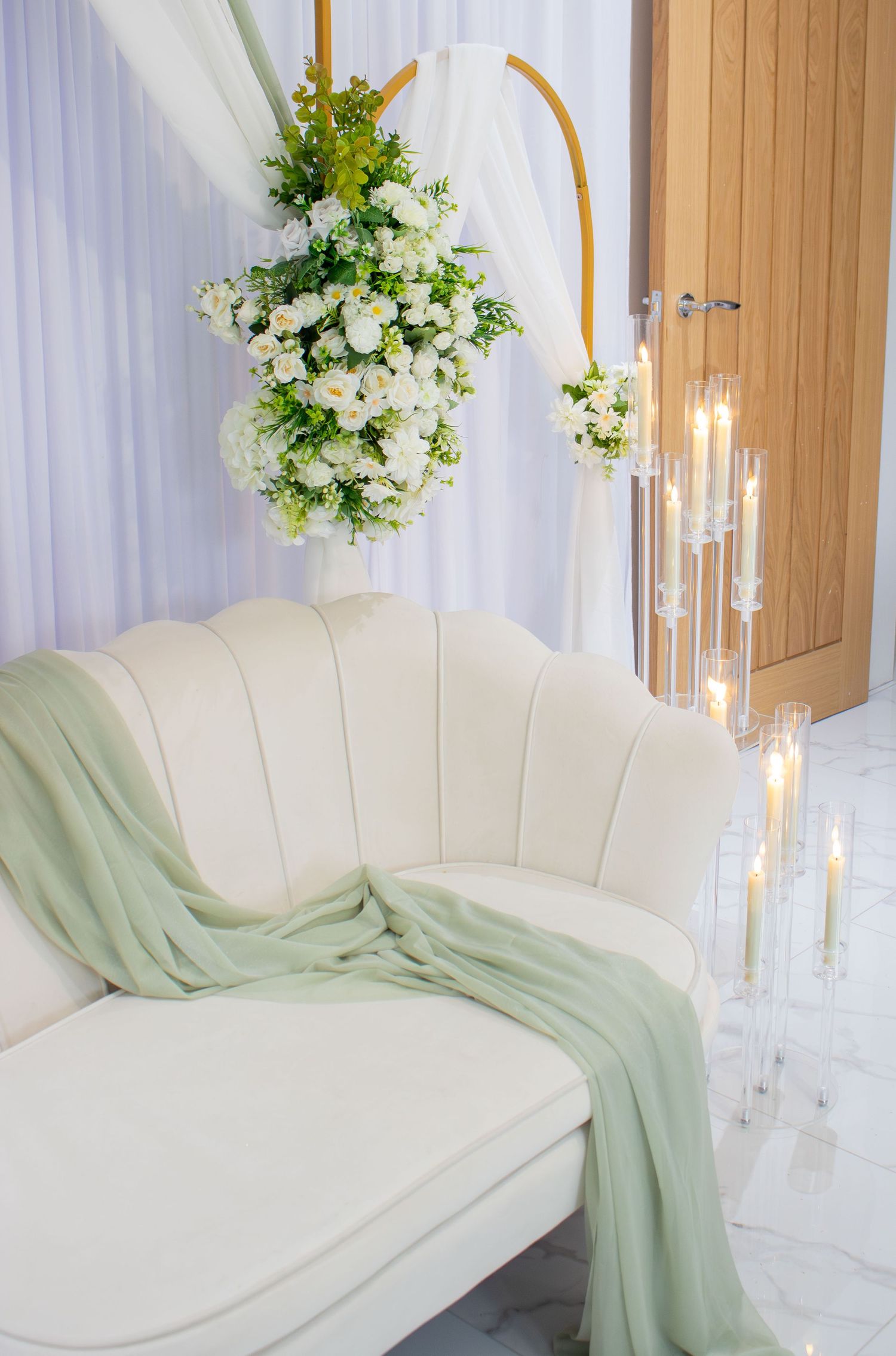 Elegant white chaise lounge with mint green throw blanket and hanging floral arrangements in a light-filled room.