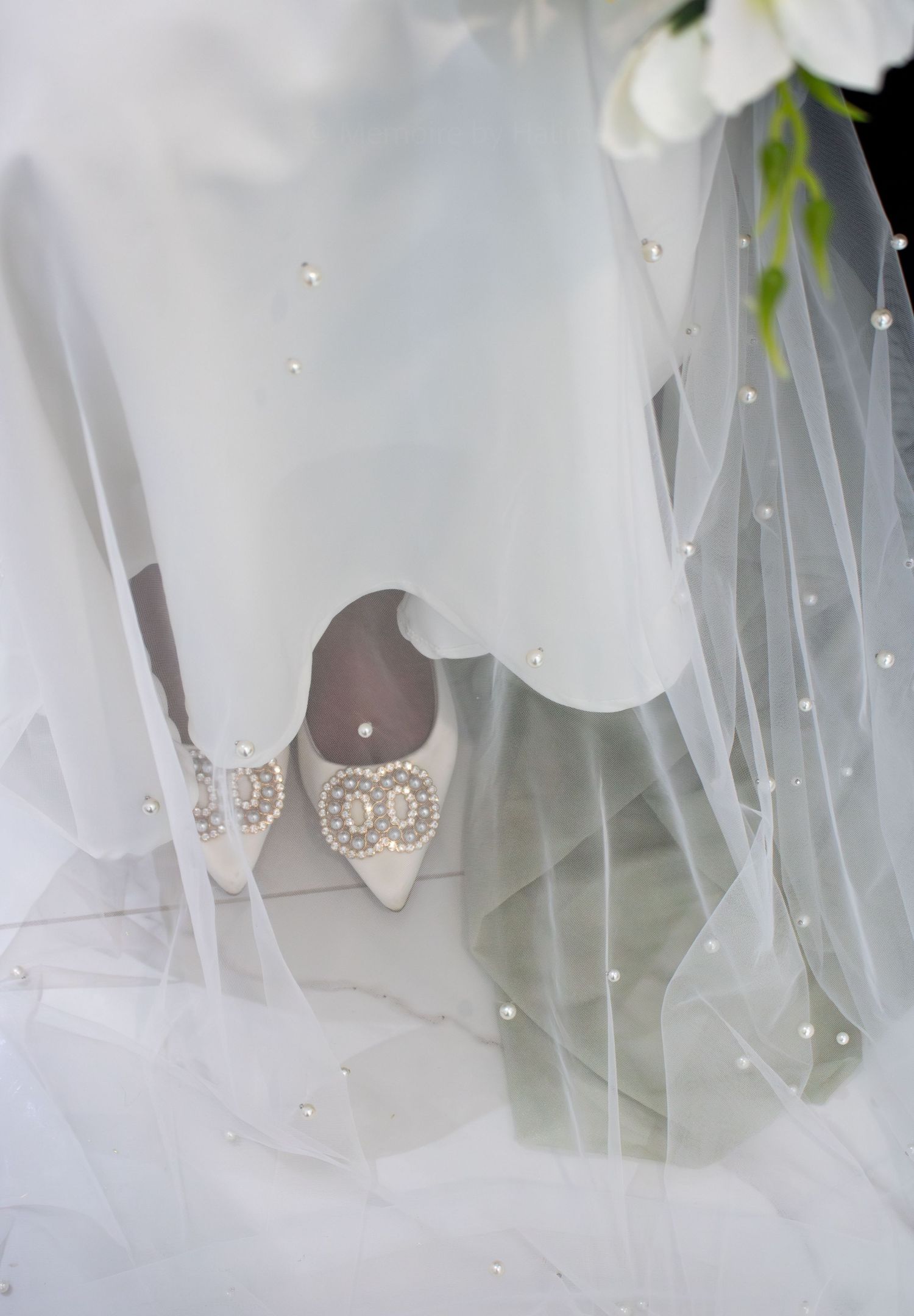 Elegant bridal shoes with delicate lace details peeking through flowing white tulle veil.
