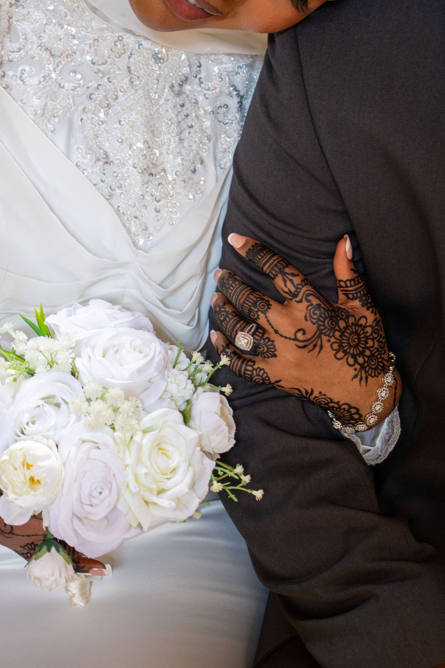 Wedding photo showing intricate henna design on hand next to white rose bouquet and lace dress details.