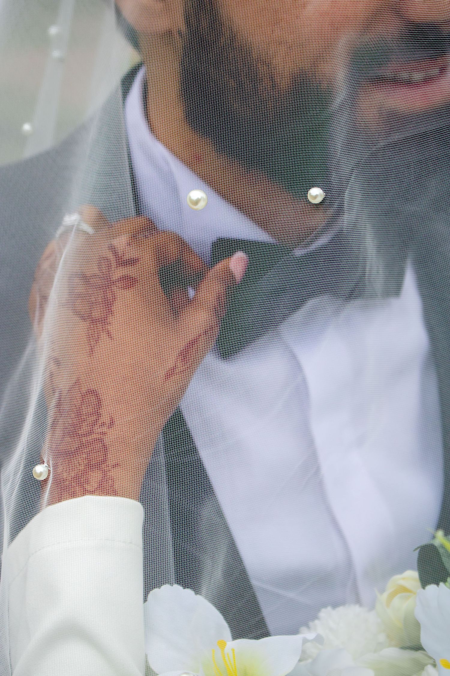 Close-up of henna-decorated hand adjusting a grey suit tie through sheer white veil.