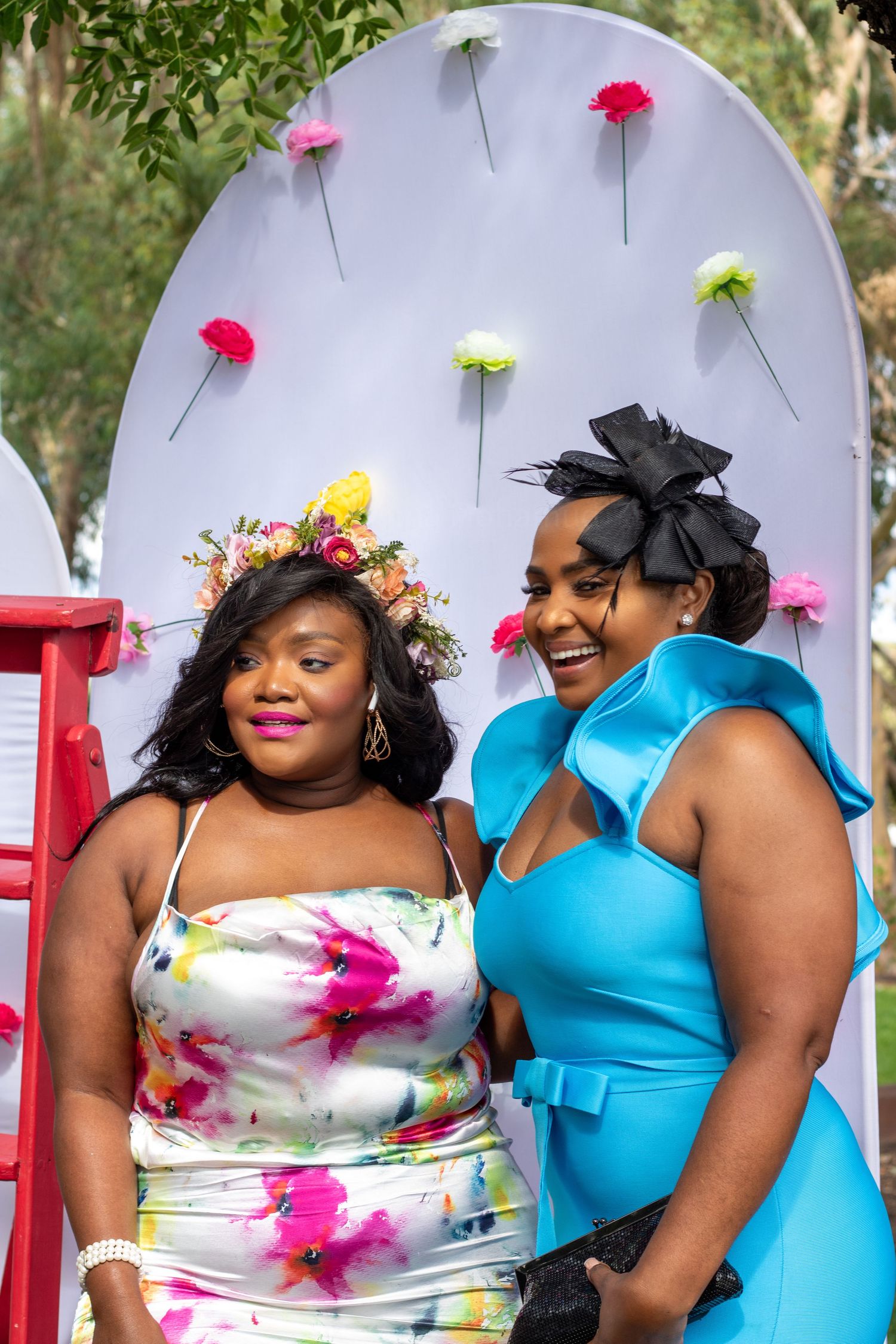Wedding party members in bright turquoise and floral dresses pose together at an outdoor celebration.