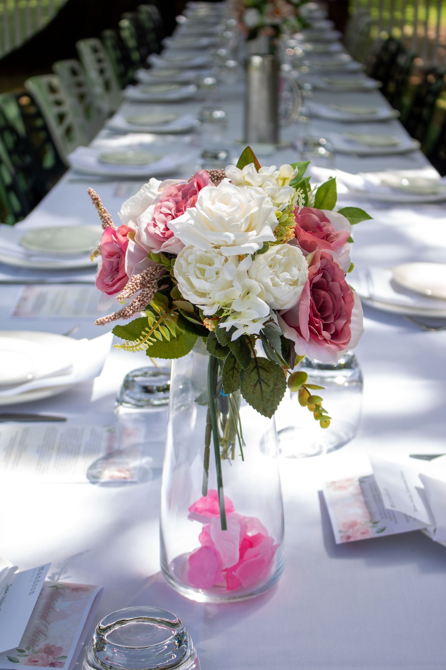 A beautiful floral centerpiece of pink and white roses adorns a long dining table set for an event.
